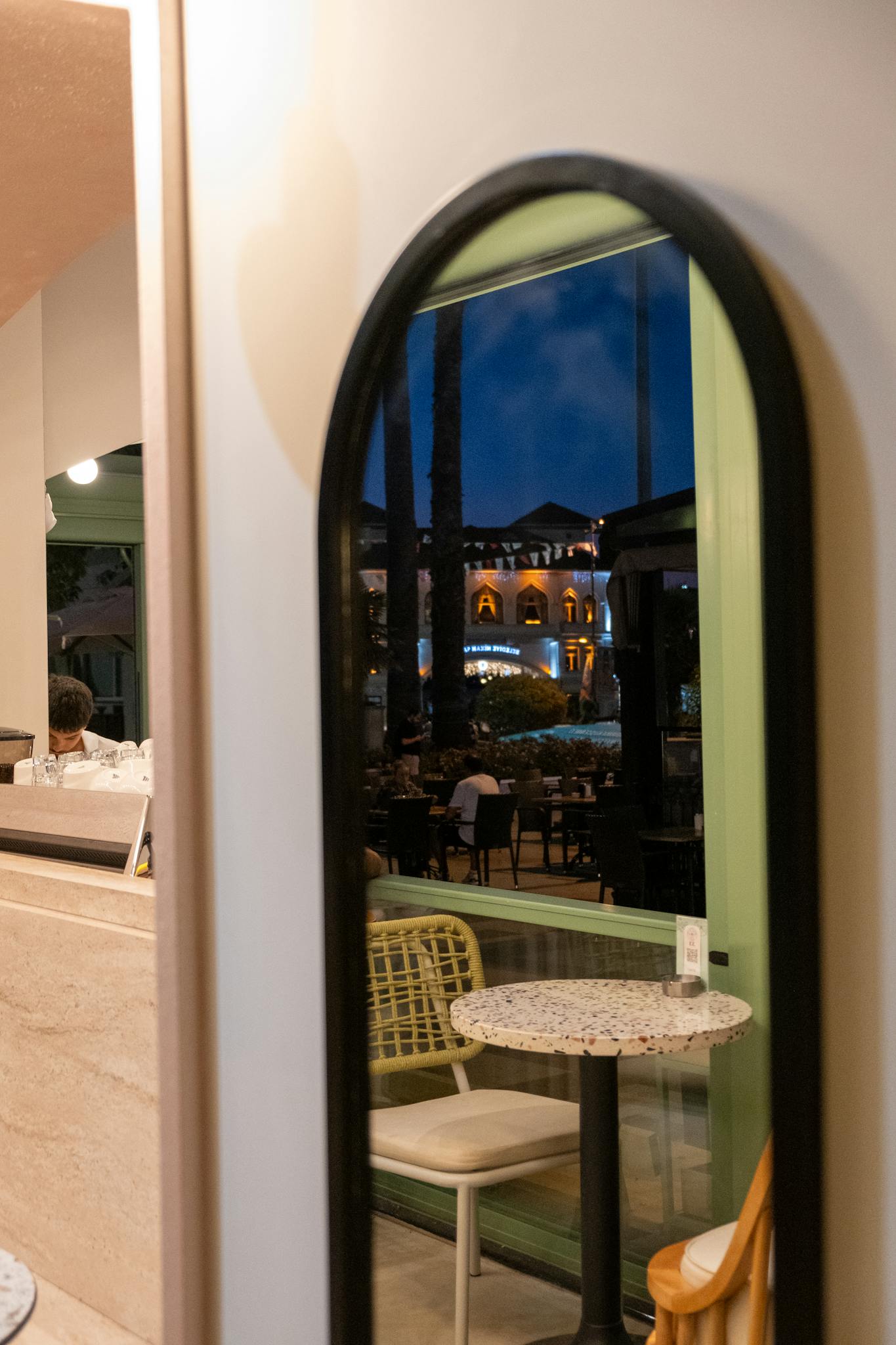 Elegant cafe setup with outdoor view reflected in mirror, creating an inviting atmosphere.