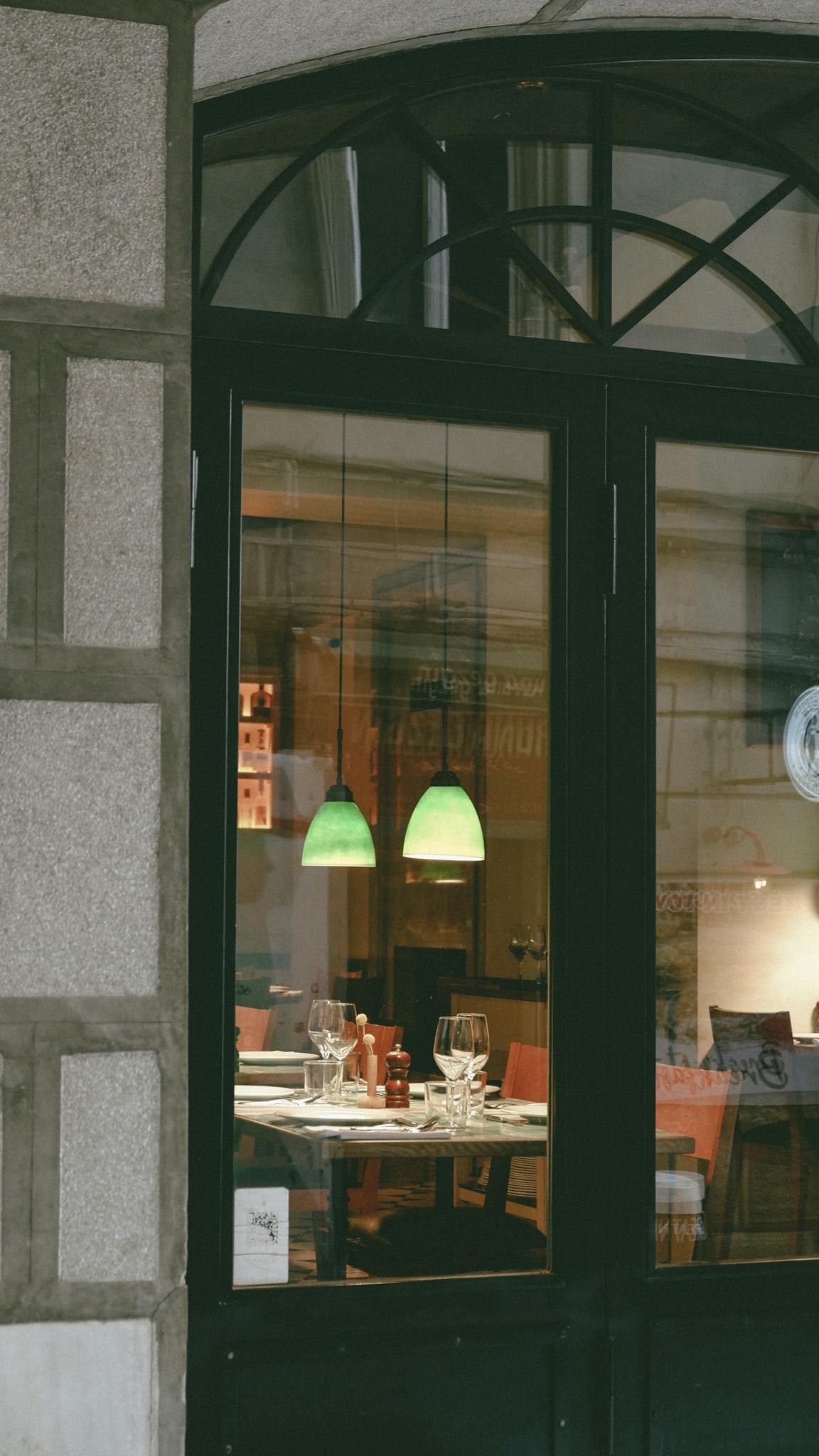 Warm and inviting restaurant interior seen through a glass door, showcasing a set dining table.